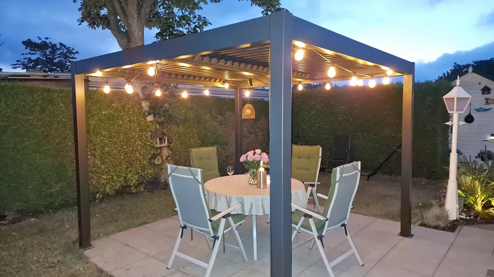 Gedeckter Tisch unter der beleuchteten Pergola im privaten Garten